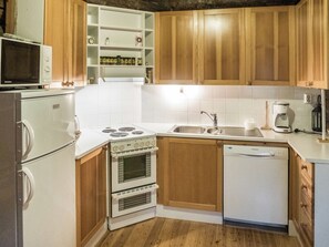 Cozinha compacta com armários de madeira, fogão branco, micro-ondas, pia e lava-louças.