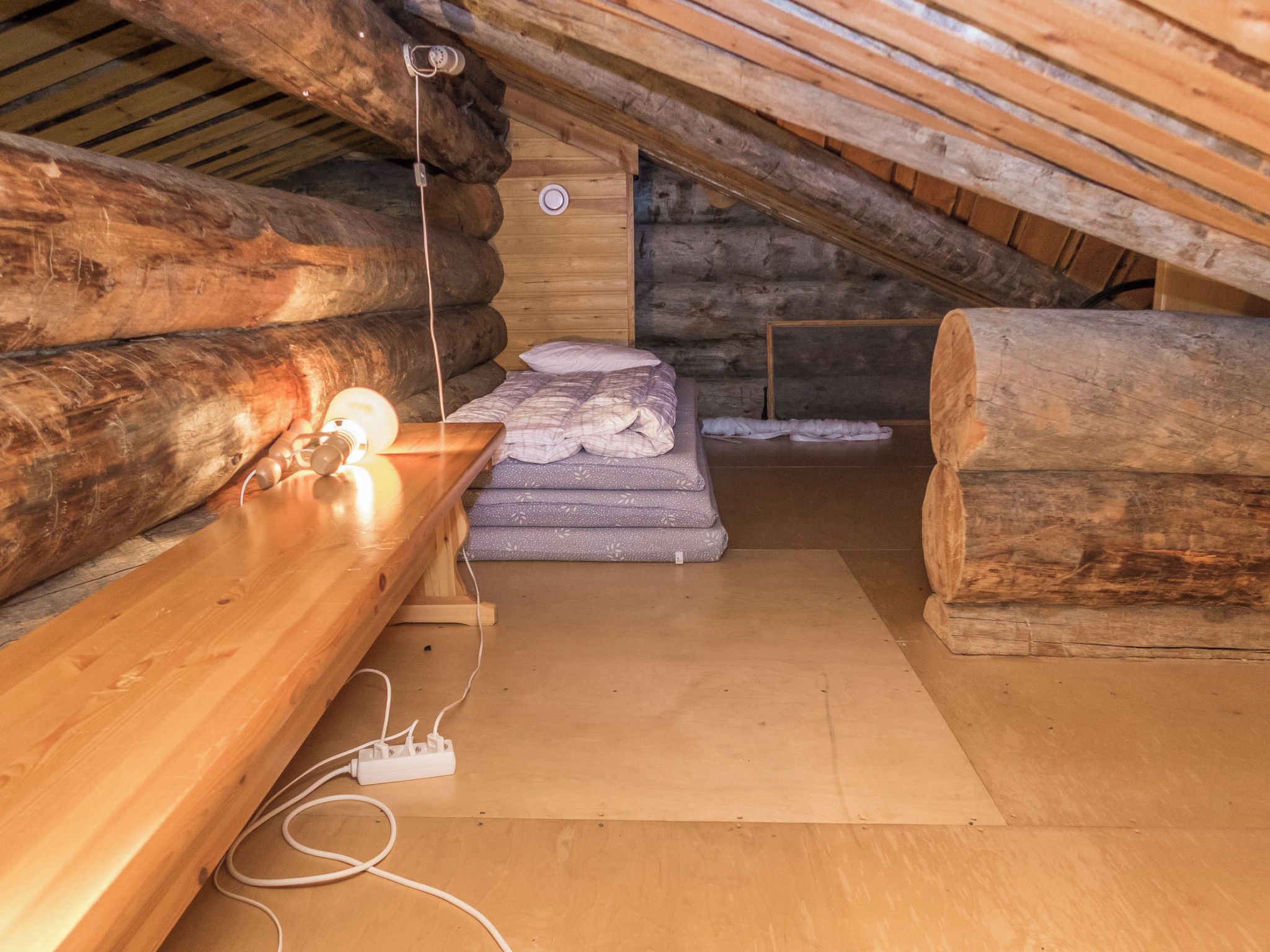 A log cabin interior with a wooden bench, a bed with pillows, and a stone wall.