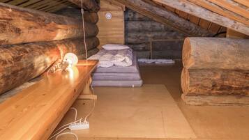 A log cabin interior with a wooden bench, a bed with pillows, and a stone wall.