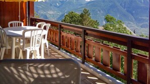 Una terraza con barandal de madera, sillas de plástico blanco y un paraguas amarillo.