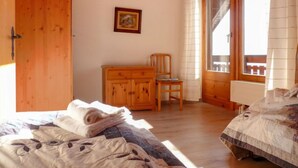 Un dormitorio con cama y cómoda de madera, una silla y un ventanal con cortinas.