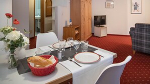 Ein Essbereich mit Tisch für zwei Personen, einer Holzkommode, einem Fernseher und einer Couch in einem Raum mit rotem Teppich.