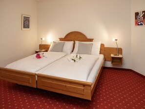 Un lit double avec une tête de lit et un pied de lit en bois, deux tables de chevet avec des lampes et un tapis rouge à motifs.