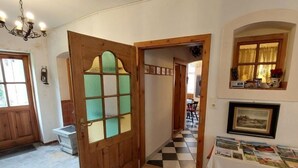 Une pièce avec une porte en bois, un lustre, un sol carrelé et une table recouverte d’une nappe blanche.