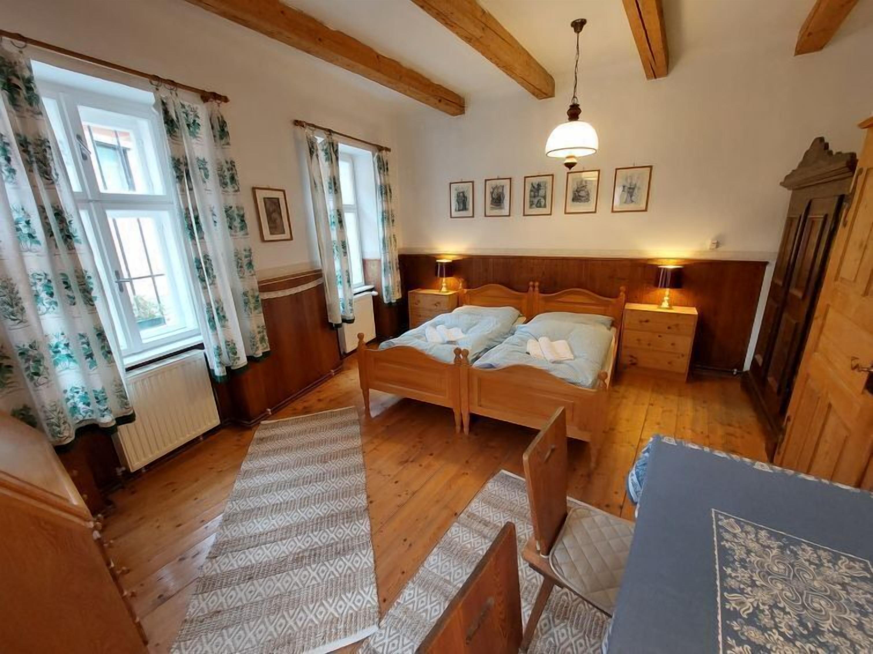 A wooden room with a bed, two bedside tables, a radiator, and a window with curtains.