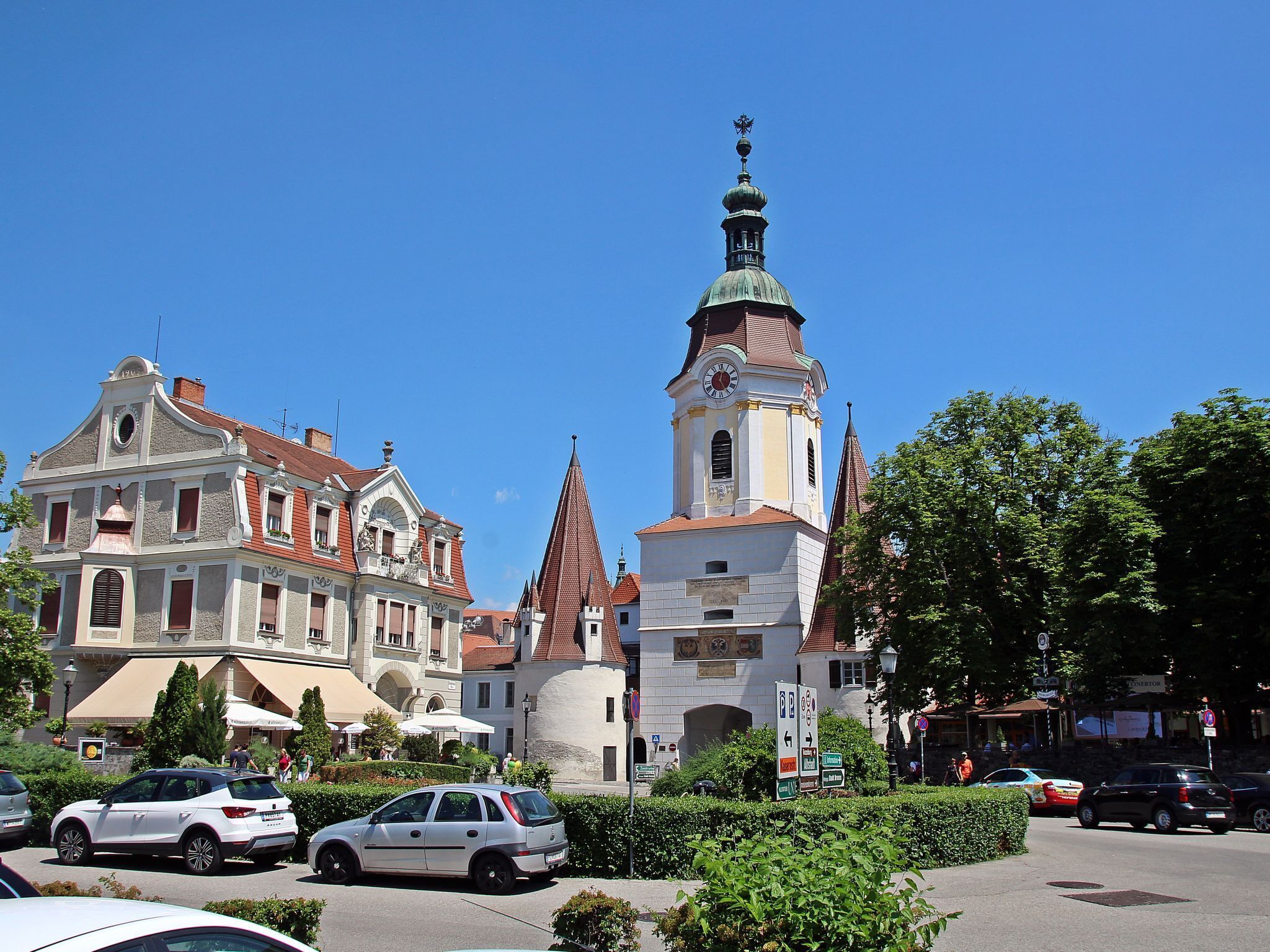 A historic building with a clock tower, surrounded by parked cars and greenery.