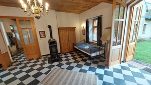 Une pièce avec un sol à carreaux, un lit avec un cadre noir, une armoire en bois, un lustre et une porte donnant sur l’extérieur.