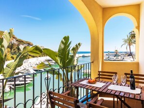 A balcony with a table, chairs, and a bottle of wine, overlooking a marina with boats and a clear blue sky.