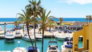 Un puerto deportivo con barcos amarrados, palmeras y un edificio con letreros.