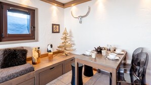 Une pièce chaleureuse avec un banc en bois, un petit sapin de Noël, une table dressée avec des tasses et une théière, et une fenêtre donnant sur la mer.