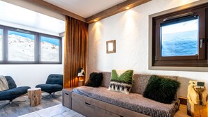 Un salon moderne avec un canapé, des fauteuils, une table basse en bois et une grande fenêtre donnant sur un paysage enneigé.