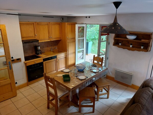A kitchen with wooden cabinets, a dining table, chairs, a coffee maker, and a hanging light fixture.