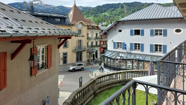 Ein Hotel mit einer Uhr, einem Balkon und Bergblick.