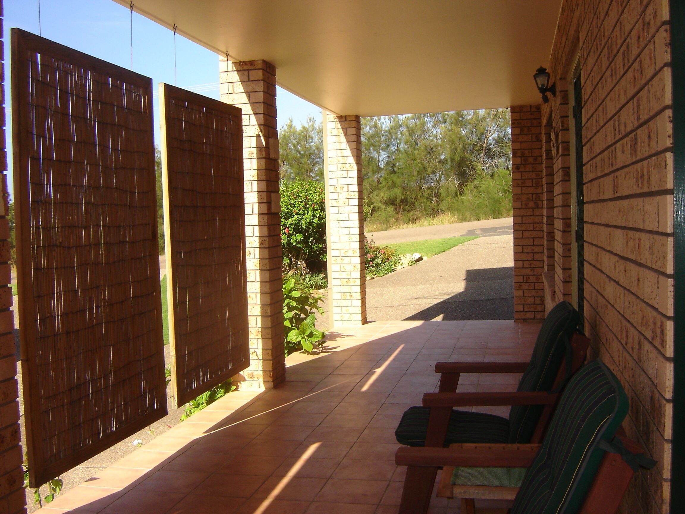 A covered patio area with a brick wall, a wooden fence, and a bench.