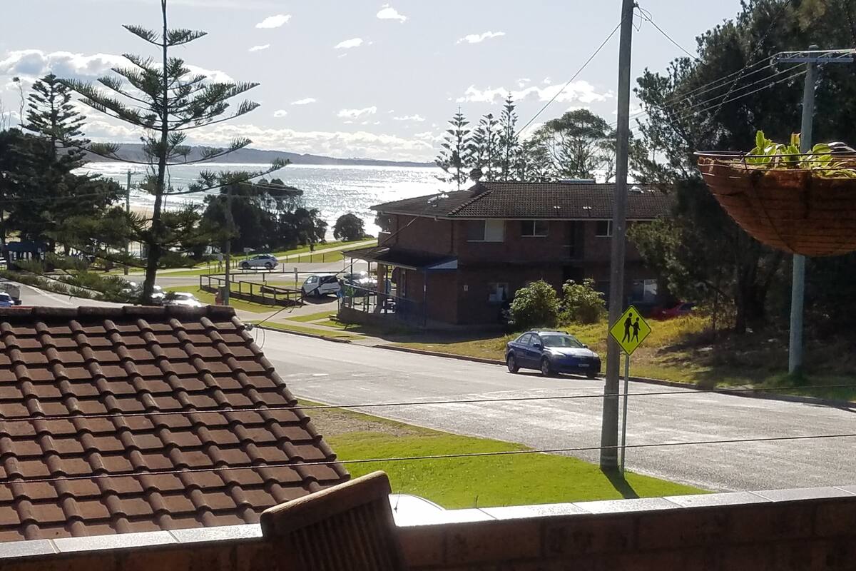 Une rue résidentielle avec des toits recouverts de tuiles, un panneau indiquant un passage piéton et une vue sur la mer.