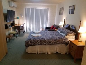 Une chambre d’hôtel avec un grand lit, un bureau avec une chaise, un téléviseur fixé au mur et une fenêtre avec des stores.