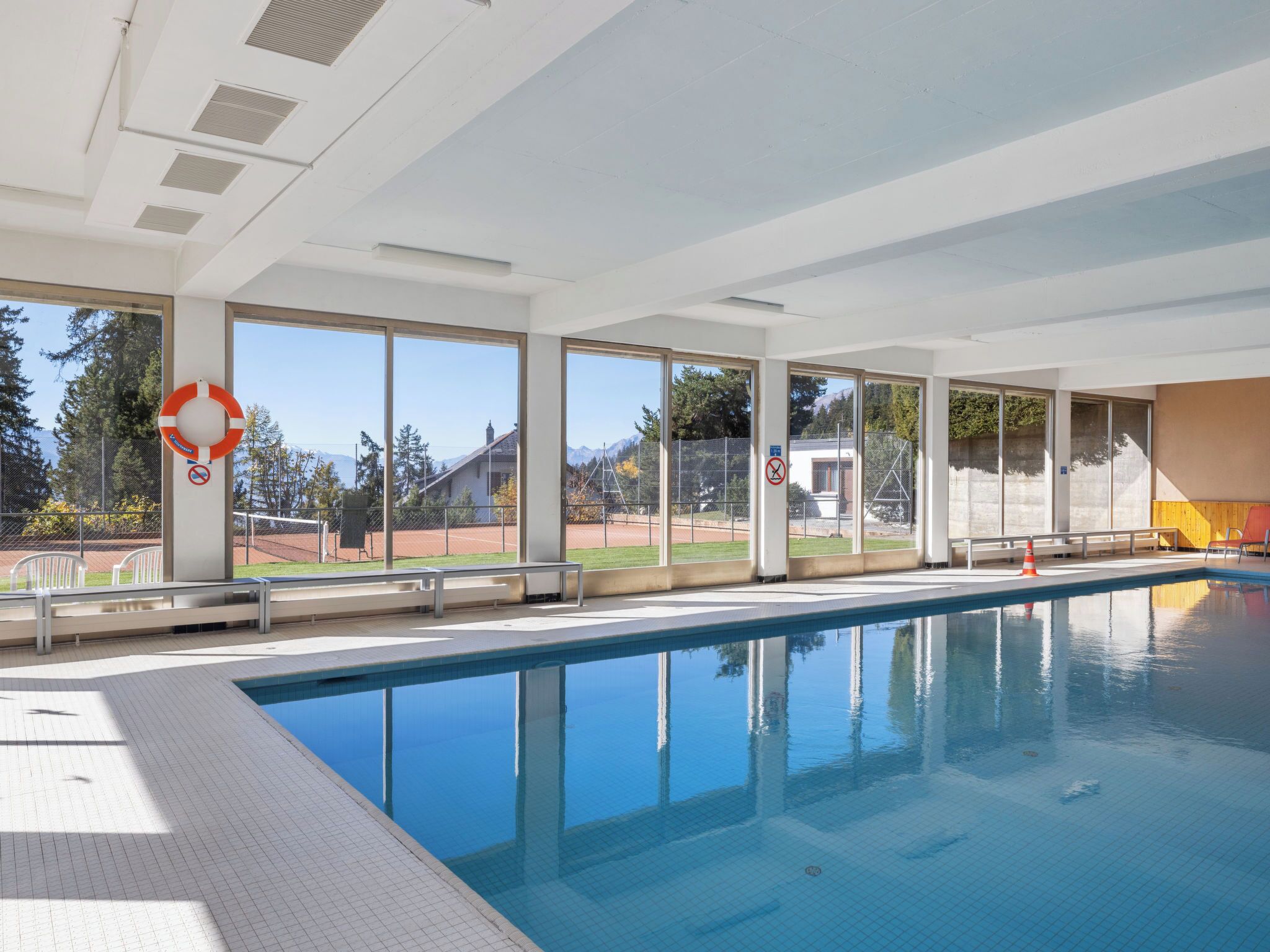 Une piscine offrant une vue dégagée sur l’extérieur, notamment sur un court de tennis et une montagne en arrière-plan.