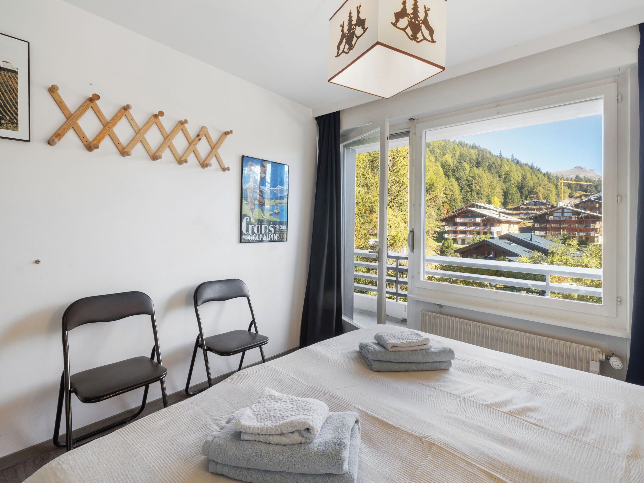 A hotel room with a bed, two chairs, a poster, and a view of a mountainous area.