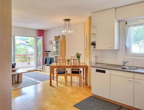 Une cuisine moderne avec des meubles blancs, un coin repas doté de chaises en bois et une grande fenêtre offrant une vue sur l’extérieur.
