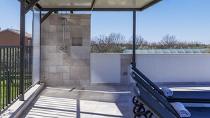 Un espace extérieur abrité, équipé d’une douche, d’un banc et offrant une vue sur le paysage environnant.