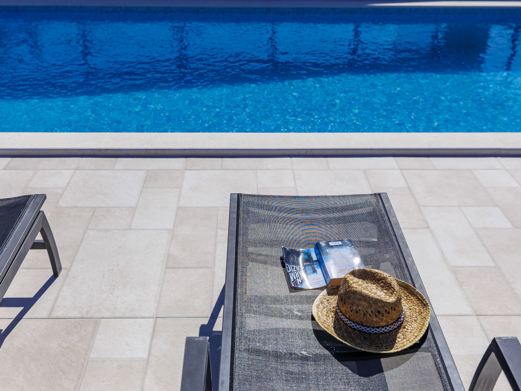 Uma área à beira da piscina com uma espreguiçadeira, um chapéu de sol e uma garrafa de água.