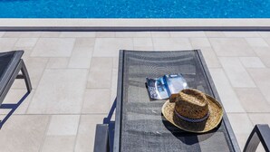 Un espace aménagé au bord de la piscine, avec une chaise longue, un chapeau de soleil et une bouteille d’eau.