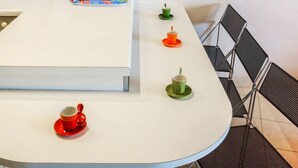 Une cuisine moderne avec un plan de travail blanc, une machine à café, une bouilloire et un ensemble de tasses et de soucoupes colorées.