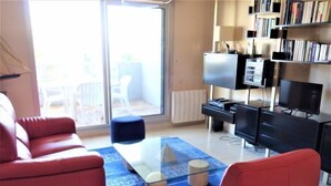 Un salon avec des canapés rouges, une table basse en verre, un tapis à motifs bleus, un téléviseur et une bibliothèque.