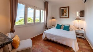 Ein Schlafzimmer mit einem Bett, zwei Nachttischlampen, einem Nachttisch, einem Sessel und einem Fenster mit Vorhängen.