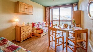A cozy room with a bed, a wooden dresser, a dining table with chairs, and a window with a mountain view. - Soyouz Vanguard by Interhome (Le Corbier)