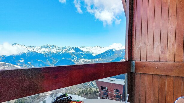 A balcony with a table, a bowl of fruit, and a view of snow-capped mountains. - Soyouz Vanguard by Interhome (Le Corbier)