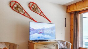 A cozy living room with a television, wooden furniture, and a window with curtains. - Rossignol C4 by Interhome (Nendaz)