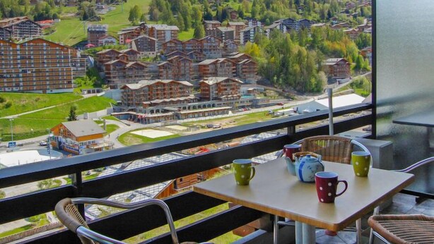 A balcony with a table and chairs overlooking a mountainous village with chalet-style buildings. - Rossignol C4 by Interhome (Nendaz)