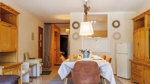 A dining area with a table set for four, wooden cabinets, a refrigerator, and a ceiling light fixture. - Rossignol C4 by Interhome (Nendaz)