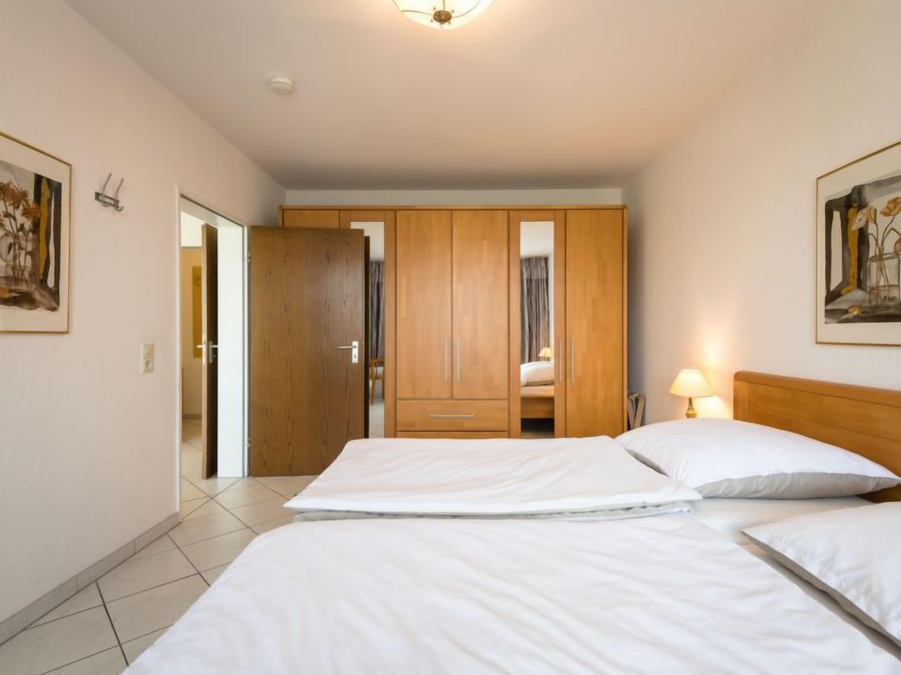 A hotel room with two beds, wooden wardrobe, and artwork on the walls.