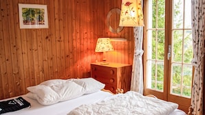 A wooden room with a bed, a dresser, a lamp, and a window with curtains.