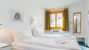 Een hotelkamer met een bed, een bureau, een stoel, een spiegel en een raam met gordijnen.