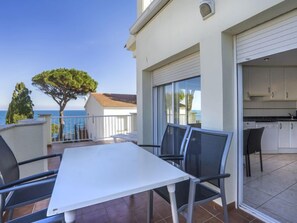 A balcony with a white table and chairs, overlooking the sea.