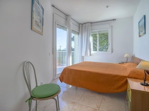 A bedroom with a bed, a chair, a desk, and a window with curtains.