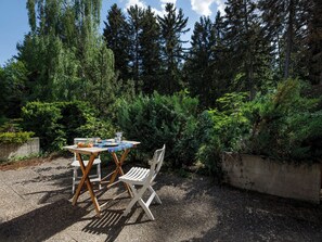Una mesa y sillas al aire libre sobre un suelo de grava, rodeado de árboles verdes y frondosos.