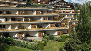 Un hotel de varios pisos con balcones, mobiliario exterior y vistas del paisaje circundante.