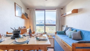 Ein gemütliches Zimmer mit einem Holztisch, einem blauen Sofa und einem großen Fenster mit Blick auf die Berge.
