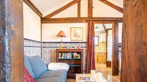 Ein gemütliches Wohnzimmer mit einer Couch, einem kleinen Tisch, einem Bücherregal und einer Küche im Hintergrund.