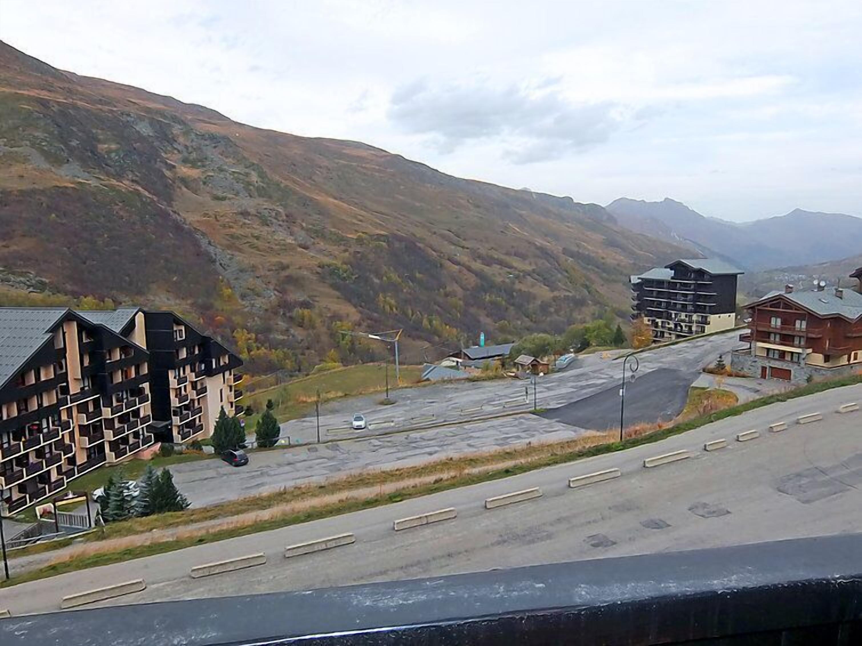 A mountain resort with multi-story buildings, a parking lot, and a road leading uphill.