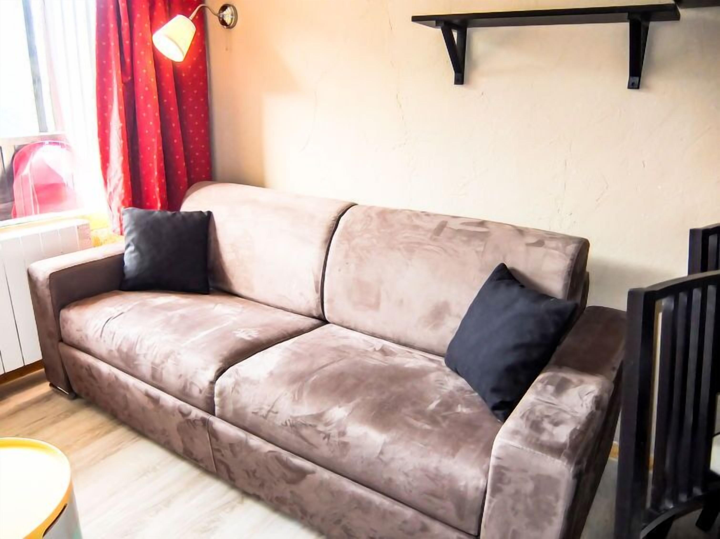 A beige sofa with a black pillow, a small table, and a wall-mounted shelf.