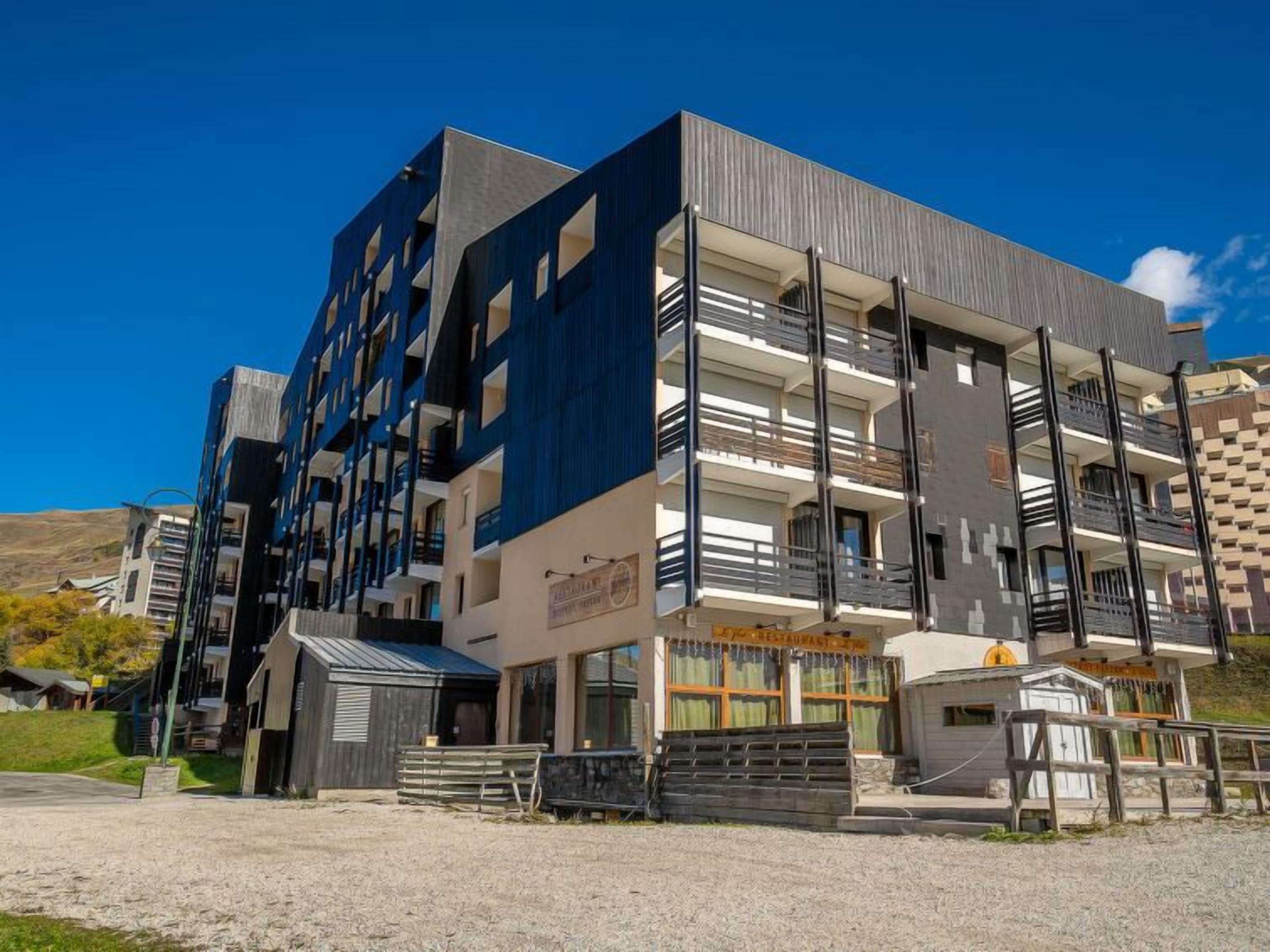 Un immeuble moderne à plusieurs étages, doté de balcons, d’un restaurant et d’un petit espace extérieur aménagé pour s’asseoir.