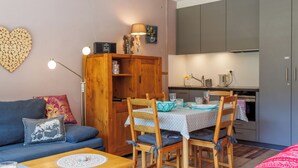 Ein kompakter Wohnbereich mit einer Couch, Esstisch, Stühlen, einem Holzschrank und einer Küchenzeile.