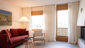 Ein Wohnzimmer mit einem roten Sofa, einem kleinen runden Tisch, einem weißen Sessel und einem Fenster mit Vorhängen.