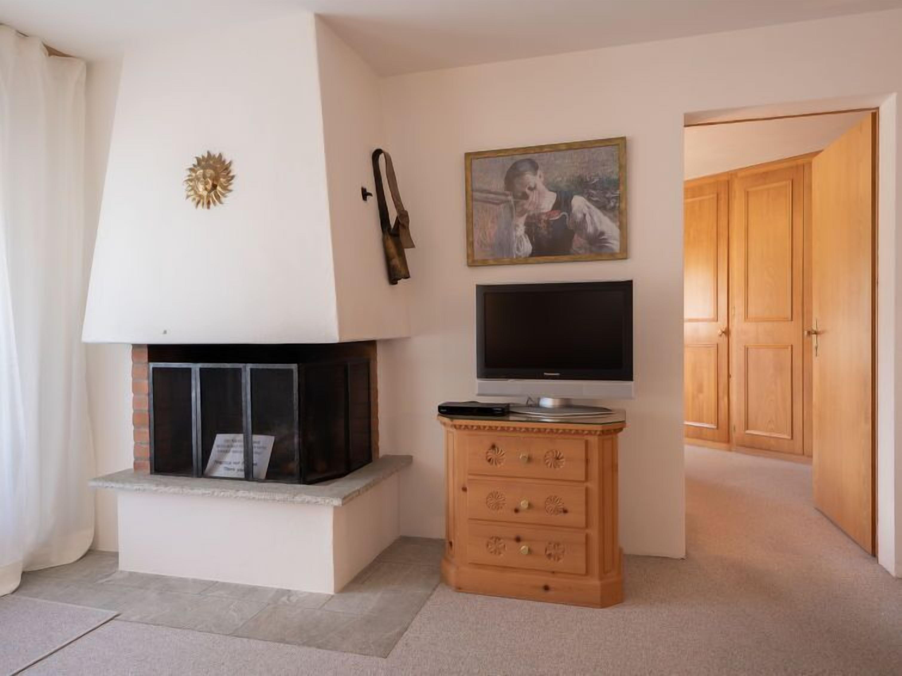 Een woonkamer met een open haard, een televisie en een houten kast.