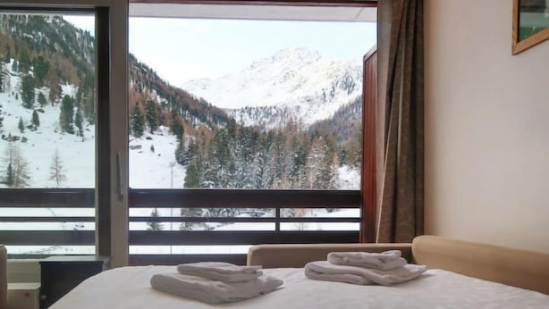 A hotel room with a bed, two folded towels, and a view of snow-covered mountains through a large window. - Rosablanche D12 by Interhome (Siviez-Nendaz)